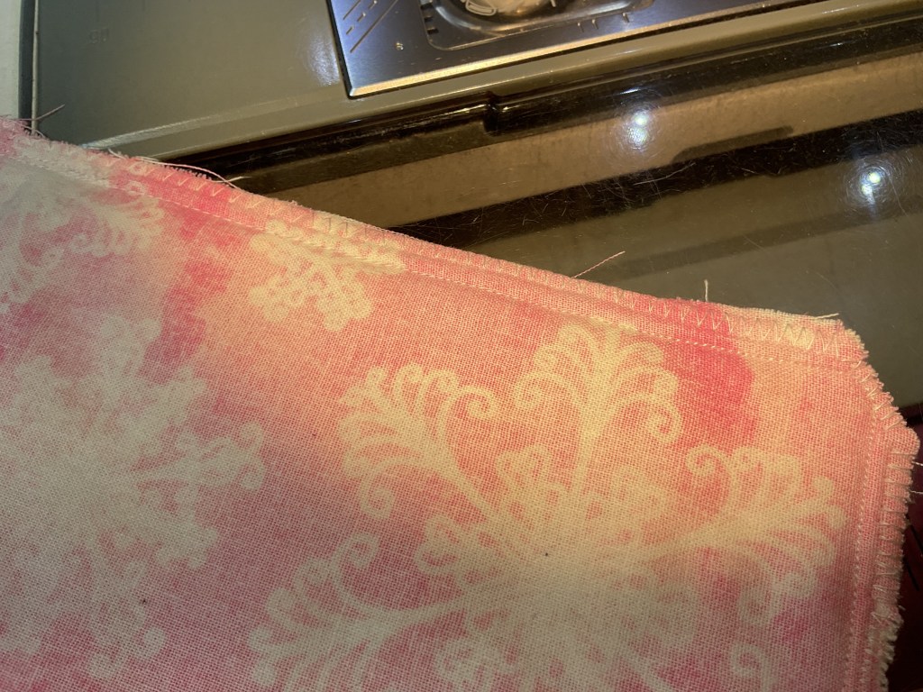 Close-up of a pink fabric with a floral pattern, partially sewn, placed on a sewing machine.