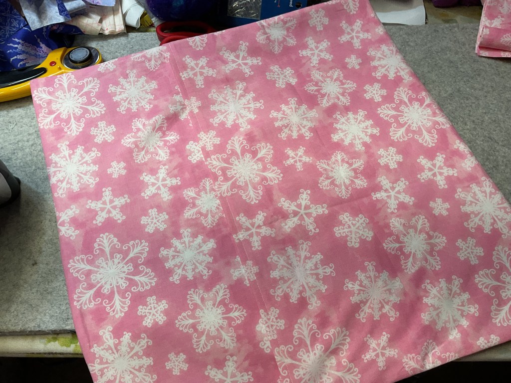 A pink fabric featuring white snowflake patterns, laid out on a workspace.