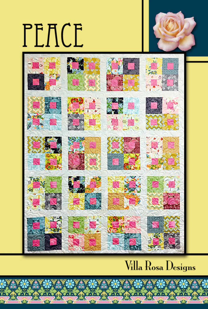 A colorful quilt titled 'Peace' by Villa Rosa Designs, featuring a grid of multi-colored patches with pink squares in the center, set against a light yellow background.