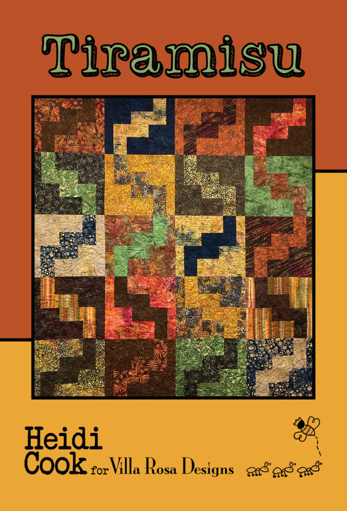 A colorful quilt titled 'Tiramisu' designed by Heidi Cook for Villa Rosa Designs, featuring a patchwork of various fabrics arranged in a zigzag pattern.