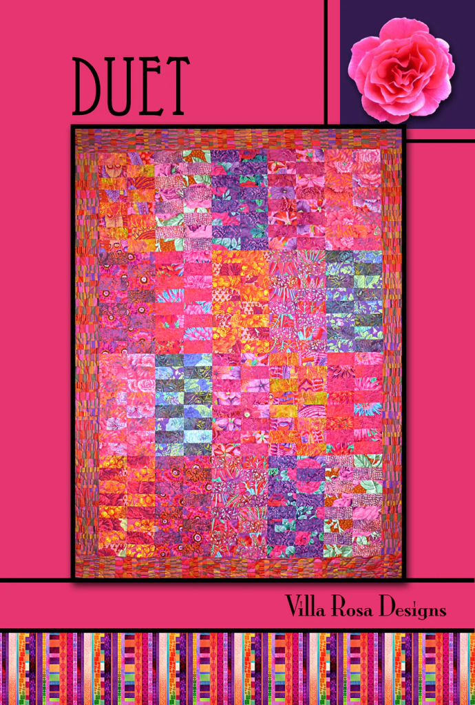 Colorful quilt titled 'Duet' by Villa Rosa Designs featuring a vibrant arrangement of pink and purple patterned fabrics.
