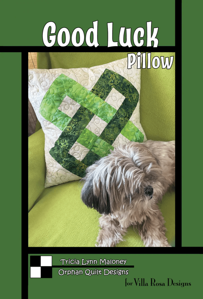 A 'Good Luck' pillow with a green shamrock design on a couch, accompanied by a small dog resting beside it.
