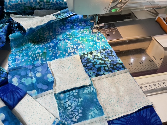 A sewing machine stitching together colorful fabric patches in shades of blue and white.