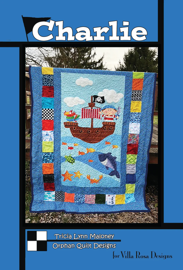 A colorful quilt featuring a pirate ship, playful sea creatures, and various patchwork patterns, designed by Tricia Lynn Maloney for Villa Rosa Designs.