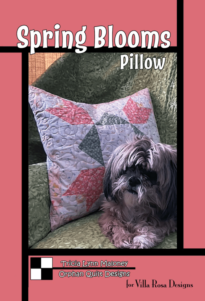 A decorative pillow titled 'Spring Blooms' displayed on a green couch, with a small dog sitting beside it.