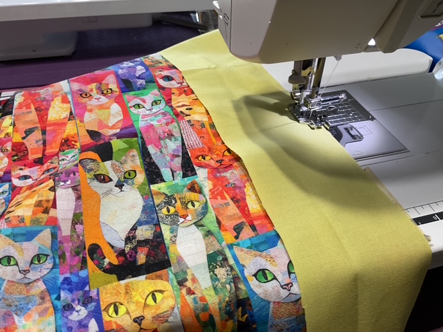 A sewing machine stitching a vibrant fabric featuring colorful cat motifs alongside a plain yellow fabric.