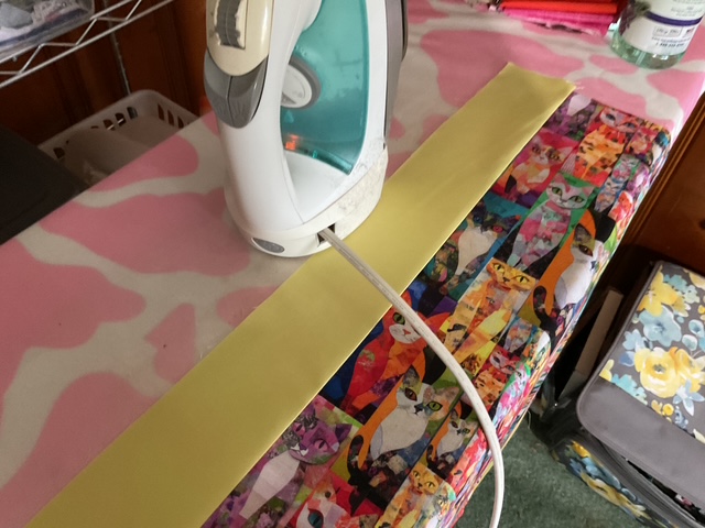 An iron resting on a colorful, patterned ironing board with a strip of yellow fabric.