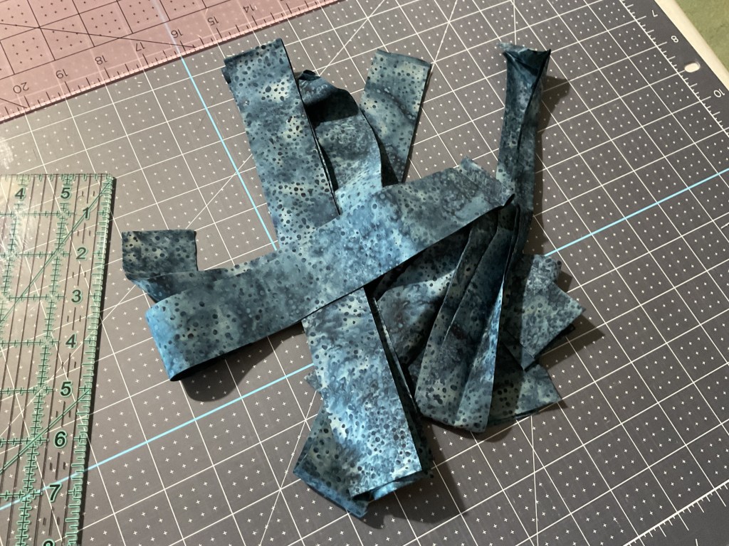 A collection of blue patterned fabric strips arranged on a cutting mat with measurement markings.