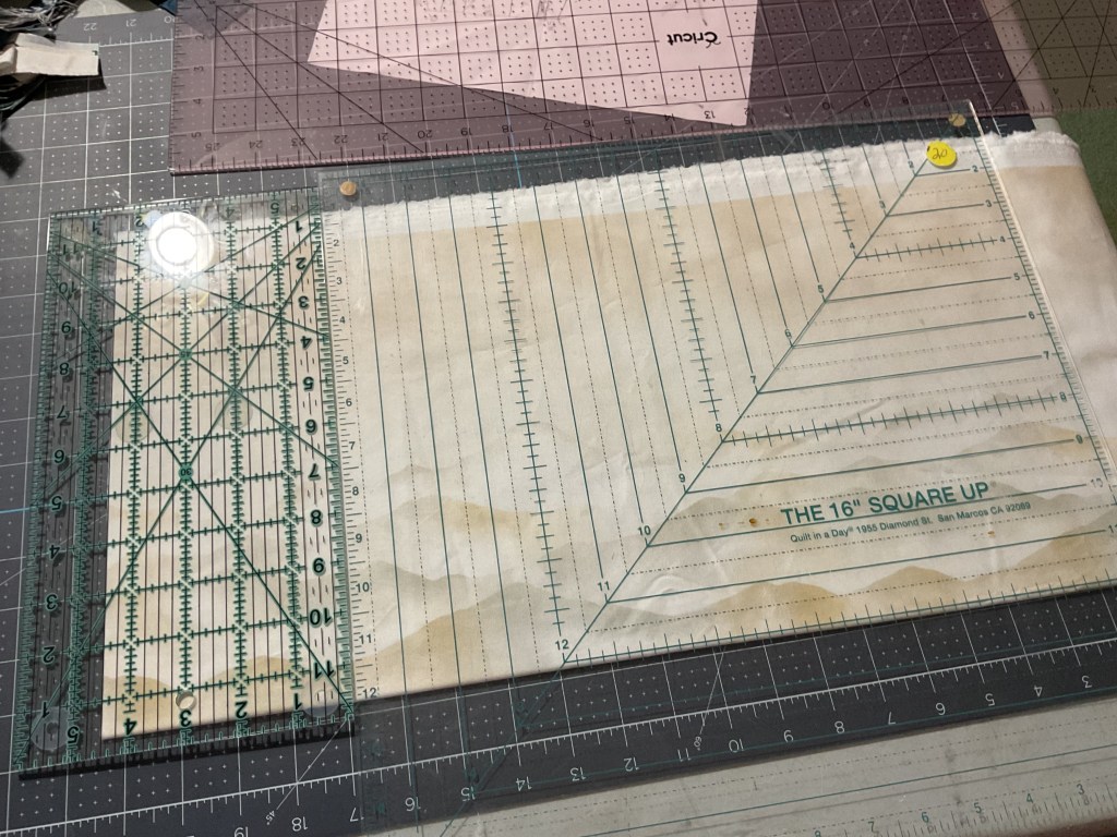 A cutting mat displaying a clear quilting ruler, marked with grid lines and measurement scales, alongside additional cutting tools and materials.