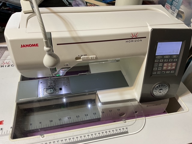 A Janome Horizon sewing machine featuring a sleek design, a digital control panel, and a clear sewing area with a ruler at the front.
