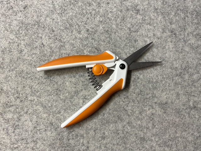 A pair of gardening scissors with orange handles and a spring mechanism, laid on a gray felt surface.