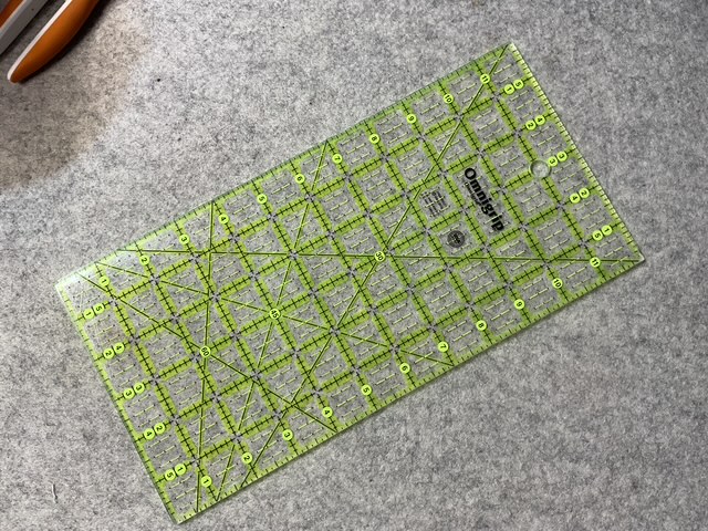 A clear quilting ruler with yellow grid lines and markings on a gray textured surface.