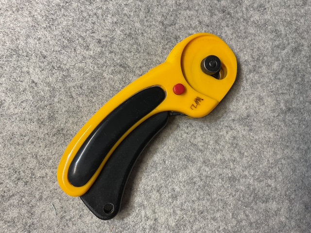 A yellow and black rotary cutter designed for fabric cutting, featuring a circular blade and a textured handle for grip.