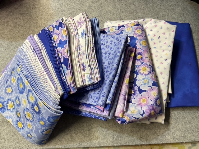 A collection of folded fabric pieces in various shades of blue and purple, featuring floral patterns.
