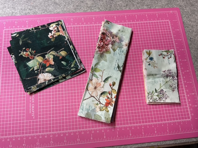 Three pieces of fabric with floral designs laid out on a pink cutting mat.