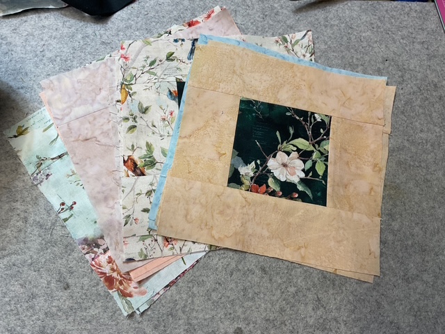 A stack of quilt fabric squares in various floral patterns, including a central square featuring a dark background with floral designs.