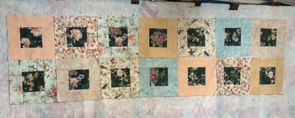A patchwork quilt layout featuring floral and pastel fabric squares arranged in a grid pattern.