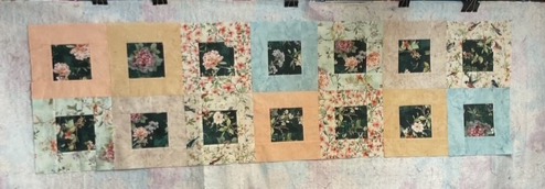 A colorful quilt layout featuring floral patterns with squares of light pastel colors and dark floral prints.