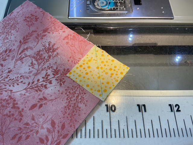 Close-up of fabric pieces, including a pink floral pattern and a yellow polka-dotted square, placed on a sewing machine table.