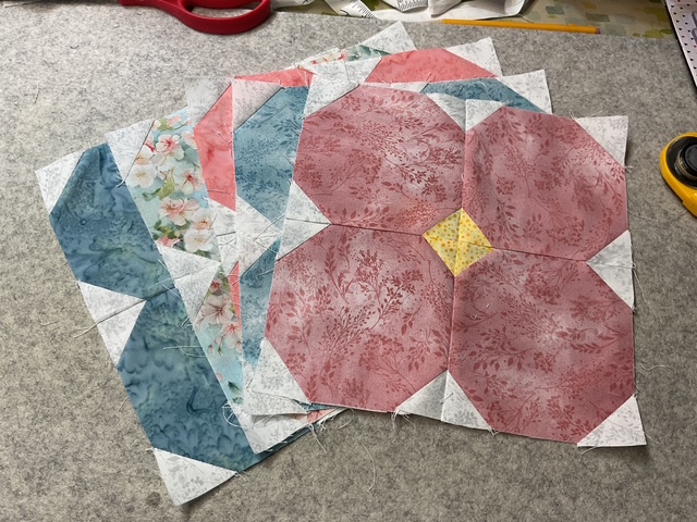 A collection of colorful quilt blocks made from various fabrics, including floral and solid patterns, arranged on a soft surface.