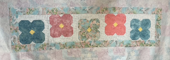 A patchwork design featuring four large flower motifs in pink, red, and blue against a light floral background.