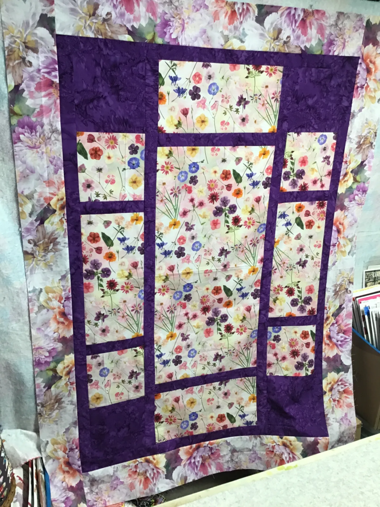 A colorful floral quilt featuring a variety of flower patterns framed with purple fabric.