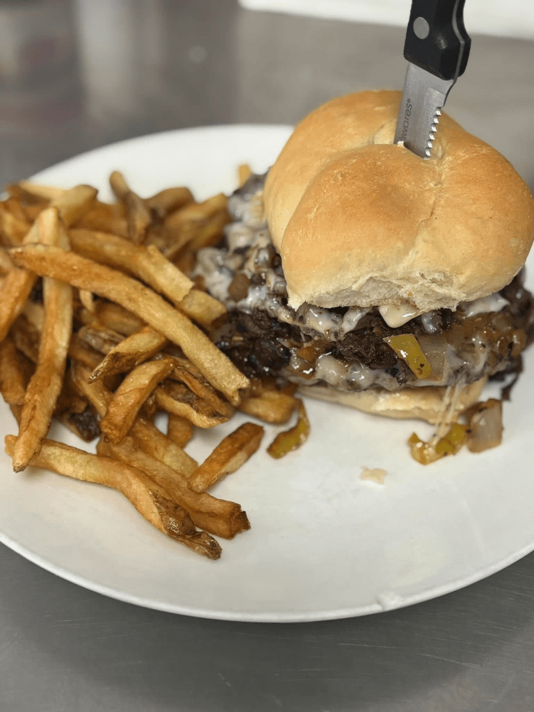 A plate featuring a sandwich filled with beef, melted cheese, and sautéed onions, accompanied by a side of golden French fries.