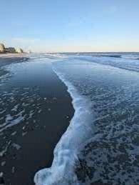 A serene view of a beach at sunset, with gentle waves lapping at the shore and a clear blue sky.