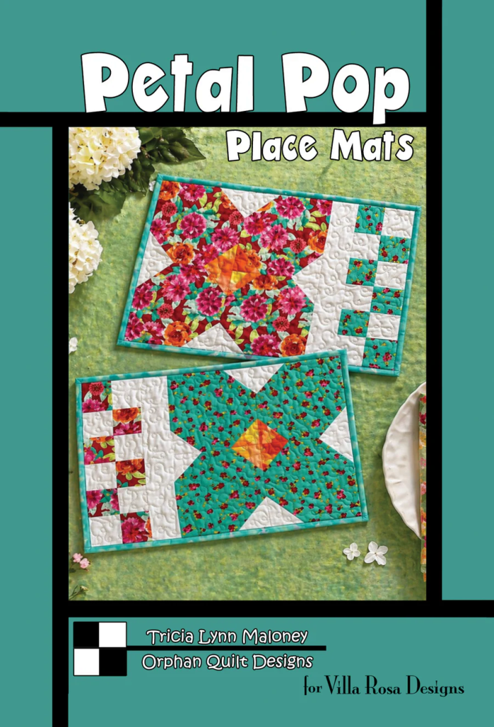 A colorful display of two quilted place mats featuring floral patterns and geometric designs, titled 'Petal Pop Place Mats', designed by Tricia Lynn Maloney for Villa Rosa Designs.