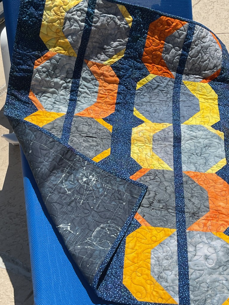 A vibrant quilt displaying geometric patterns in shades of orange, yellow, gray, and blue, folded on a blue lounger.