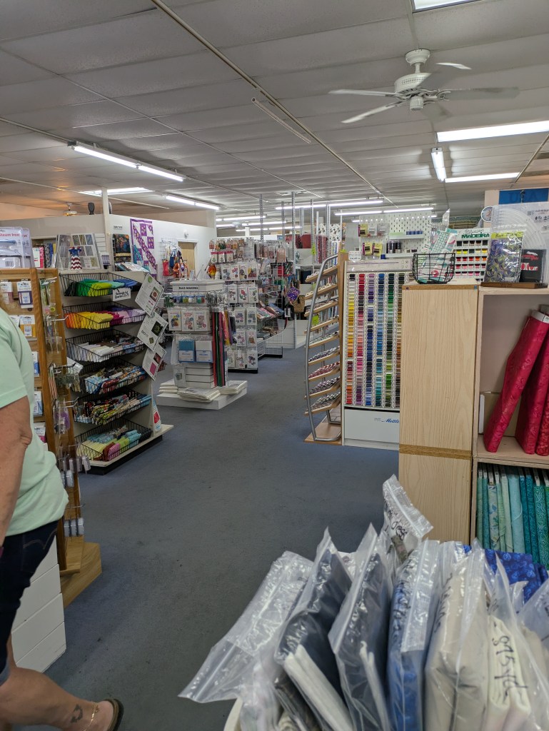 Interior view of a craft and fabric store, showcasing various colorful craft supplies, fabrics, and sewing materials displayed on shelves and racks.