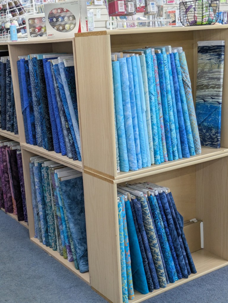Shelves displaying various blue and purple fabric rolls in a craft store.
