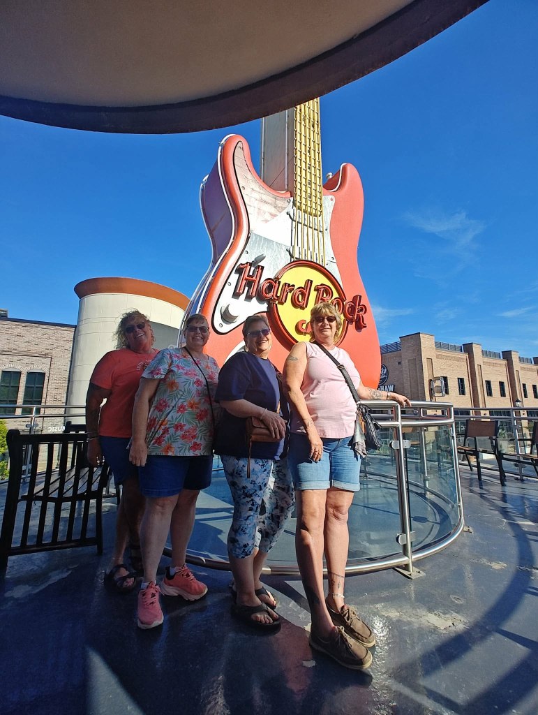 Four women posing in front of a large Hard Rock Cafe guitar sign on a sunny day.
