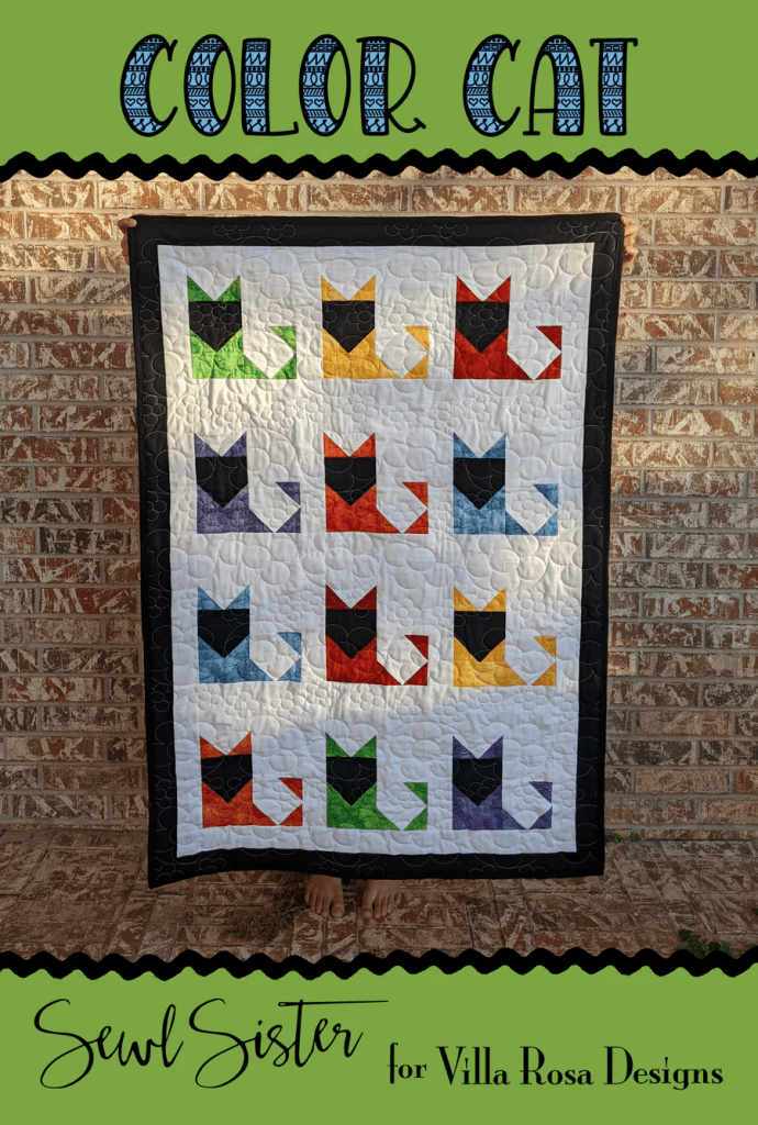 A colorful quilt featuring cat designs in various colors, displayed against a brick wall, with text at the top reading 'COLOR CAT' and additional branding at the bottom.