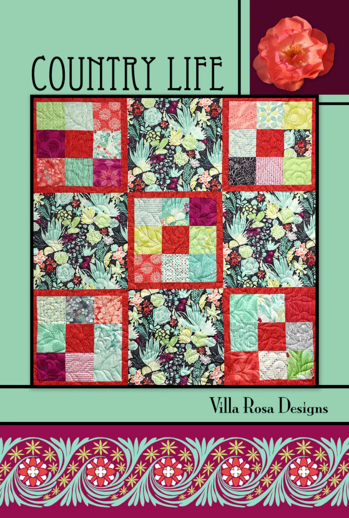 A colorful quilt titled 'Country Life' featuring various floral and geometric patterns, bordered with a decorative design by Villa Rosa Designs.