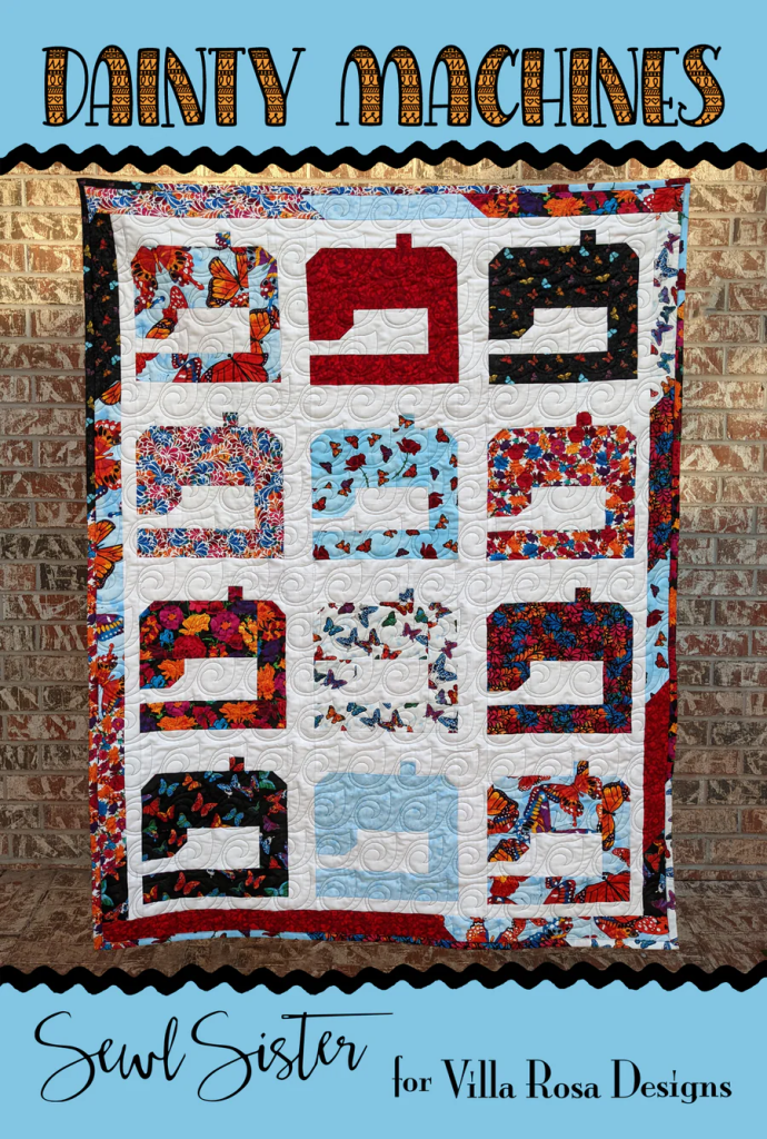 A colorful quilt titled 'Dainty Machines' featuring various sewing machine designs surrounded by floral patterns, displayed against a brick wall.