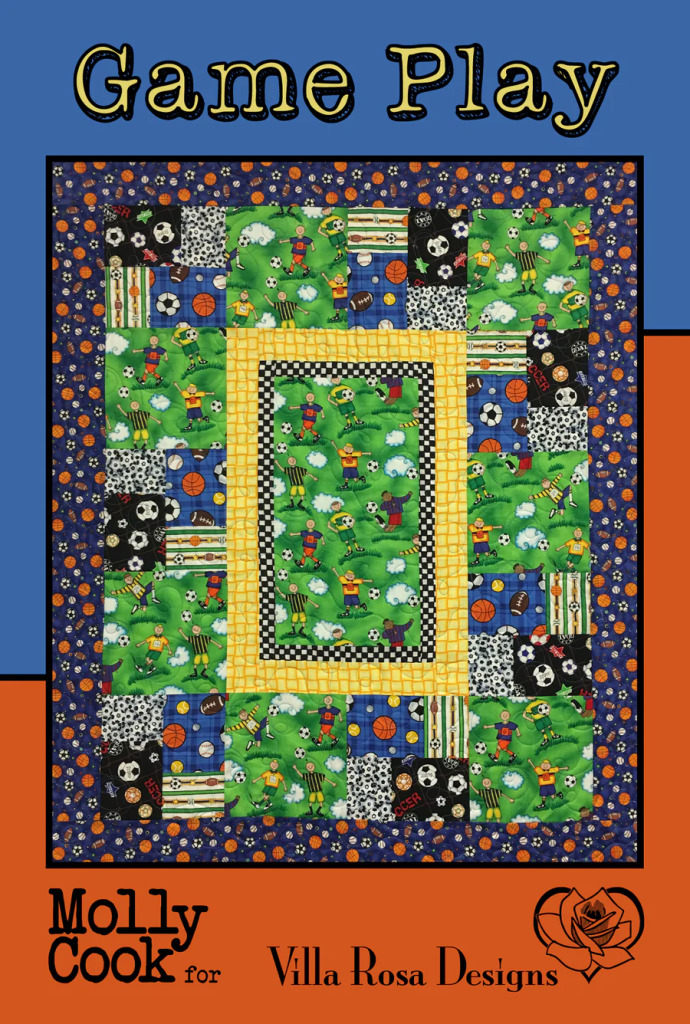 A colorful quilt titled 'Game Play' featuring sports-themed fabric squares, including soccer, basketball, and football designs, framed with a yellow border.