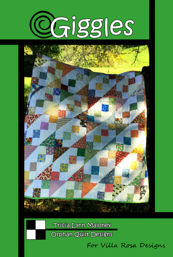 A colorful quilt featuring a patchwork design with varying patterns and colors, displayed outdoors with greenery in the background. The design is accompanied by the title 'Giggles' and credits to Tricia Lynn Maloney and Villa Rosa Designs.