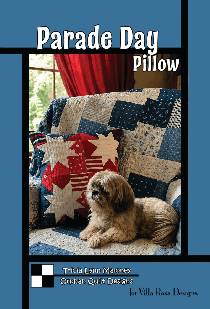 A cozy pillow design titled 'Parade Day Pillow' displayed on a blue quilted sofa, featuring a patterned quilt in shades of blue and red, with a fluffy dog resting beside it.