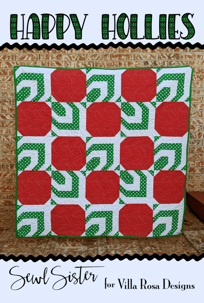 A colorful quilt titled 'Happy Hollies' displayed against a brick wall, featuring red and green patchwork designs with polka dots.