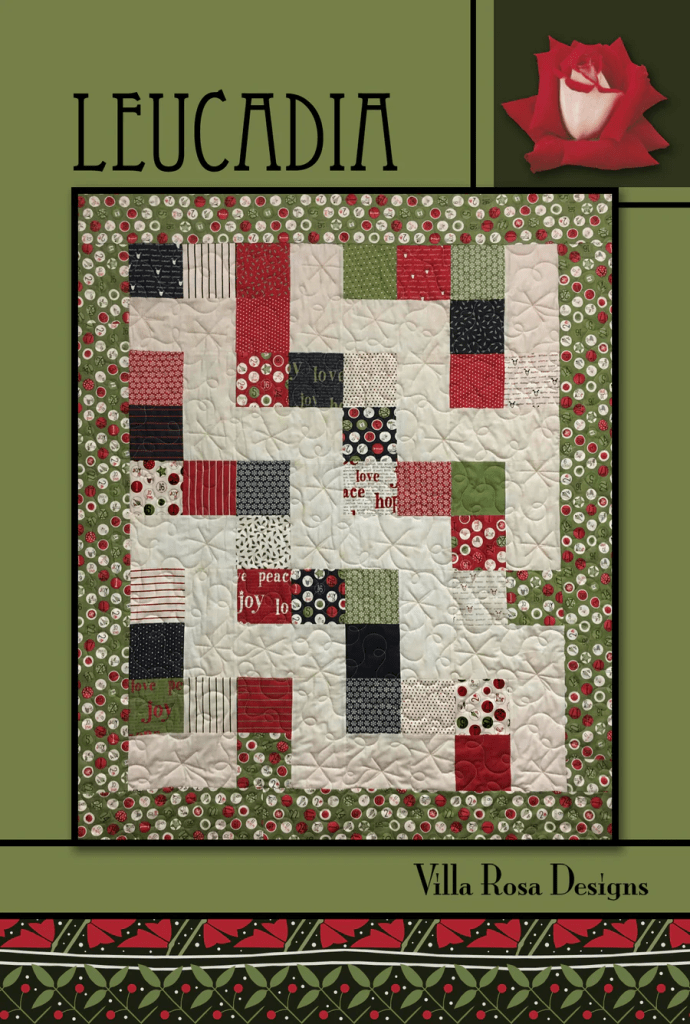 A quilt design called 'Leucadia' featuring a patchwork of red, green, and white fabrics with various patterns, bordered by a floral print. The design includes text elements like 'joy' and 'peace'.
