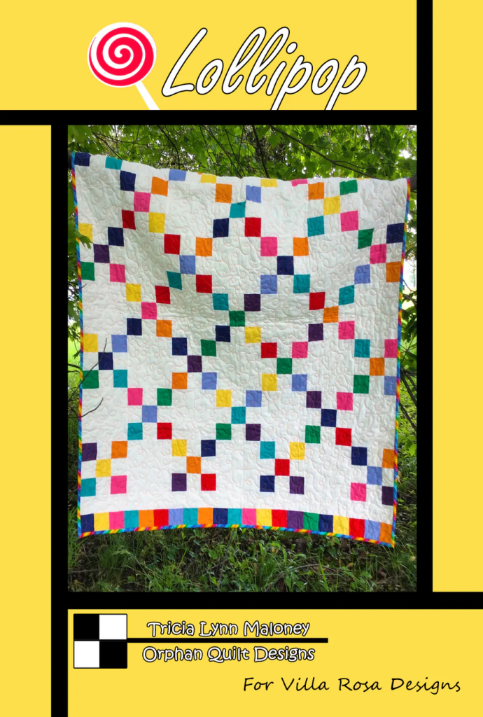 A colorful quilt design titled 'Lollipop' featuring a patchwork pattern with bright squares on a white background, displayed outdoors among greenery.