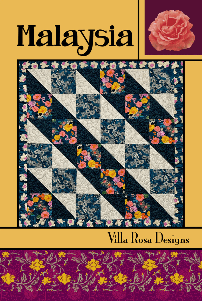 A quilt design titled 'Malaysia' featuring a patchwork pattern with dark blue and white squares, adorned with colorful floral prints. The design is framed with a decorative maroon and gold border, and includes the text 'Villa Rosa Designs' at the bottom.
