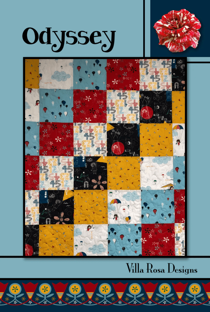 A colorful quilt design titled 'Odyssey' featuring a patchwork of various fabric patterns in red, blue, yellow, and black, with whimsical motifs including hot air balloons and flowers. The quilt is framed by a decorative border.