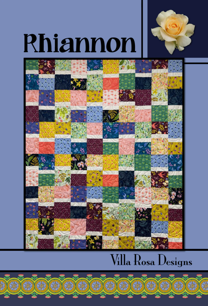 A vibrant quilt design titled 'Rhiannon' featuring a patchwork of colorful squares in various floral and geometric patterns, with a decorative border and a yellow rose in the top right corner.