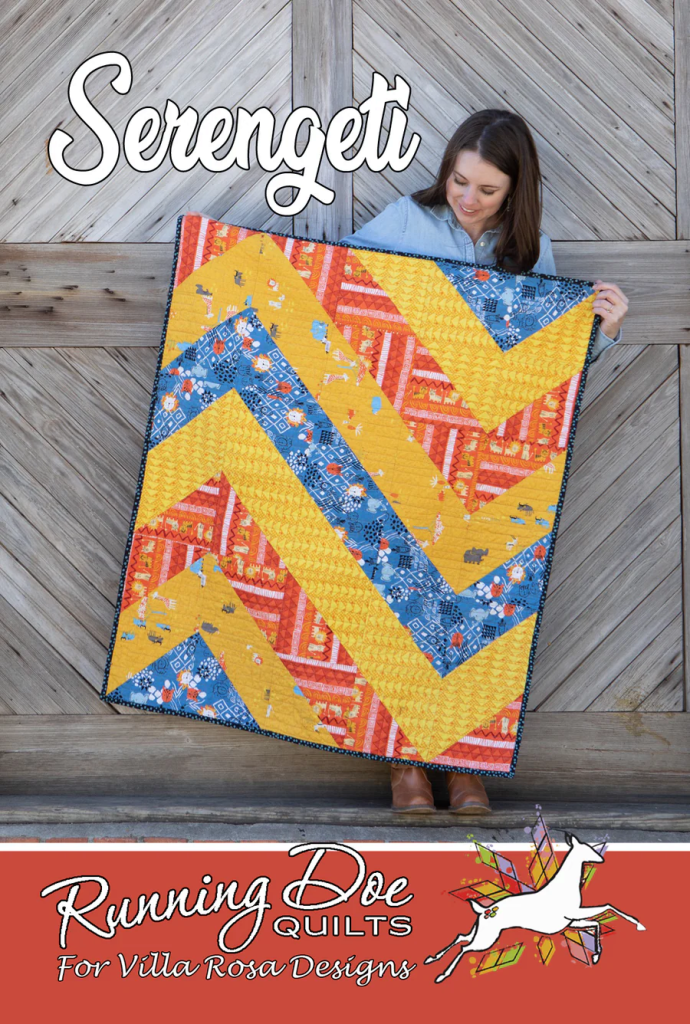 A woman holding a colorful quilt featuring a chevron pattern in yellow, orange, and blue against a wooden background. The quilt is titled 'Serengeti' and is associated with Running Doe Quilts for Villa Rosa Designs.