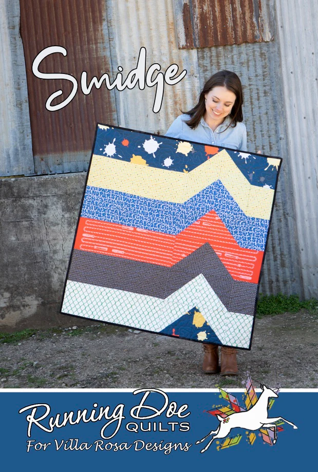 A young woman is holding a colorful quilt featuring zigzag patterns with various fabric designs, standing in front of a rustic metal backdrop. The quilt is labeled 'Smidge' and features branding for Running Doe Quilts.