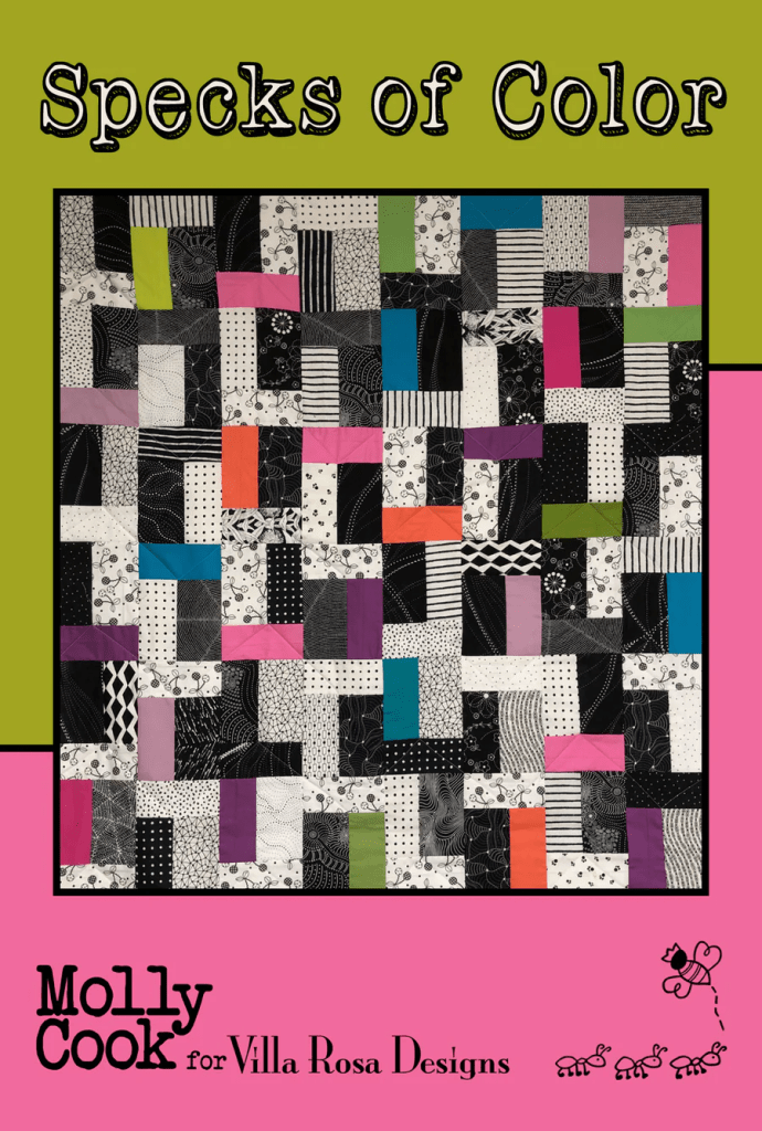 A colorful quilt featuring various patches in bright colors like pink, green, blue, and orange mixed with black and white patterns, titled 'Specks of Color' by Molly Cook for Villa Rosa Designs.
