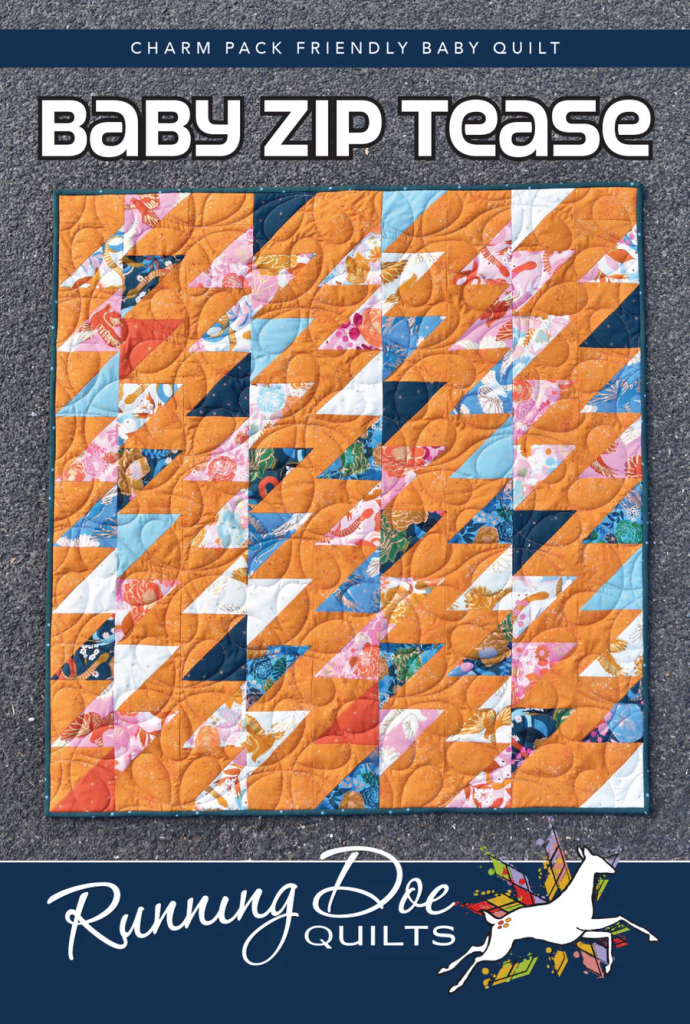 A colorful baby quilt titled 'Baby Zip Tease' featuring a zigzag pattern with shades of orange, blue, pink, and floral designs, displayed on a textured surface.