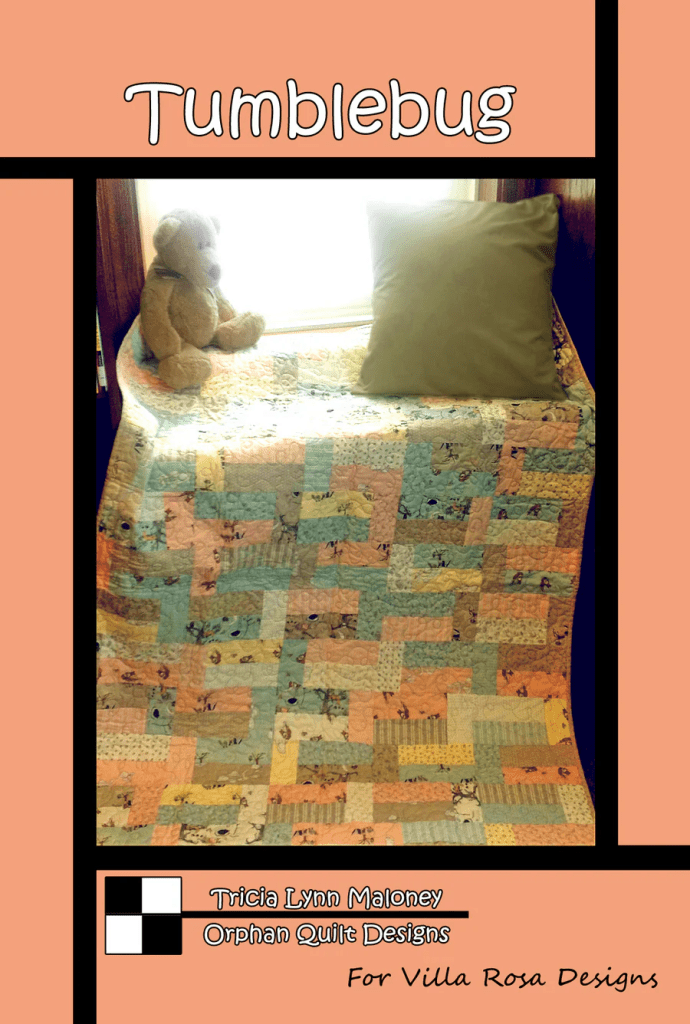 A cozy quilt titled 'Tumblebug' displayed on a bench near a window, accompanied by a stuffed bear and a decorative pillow.